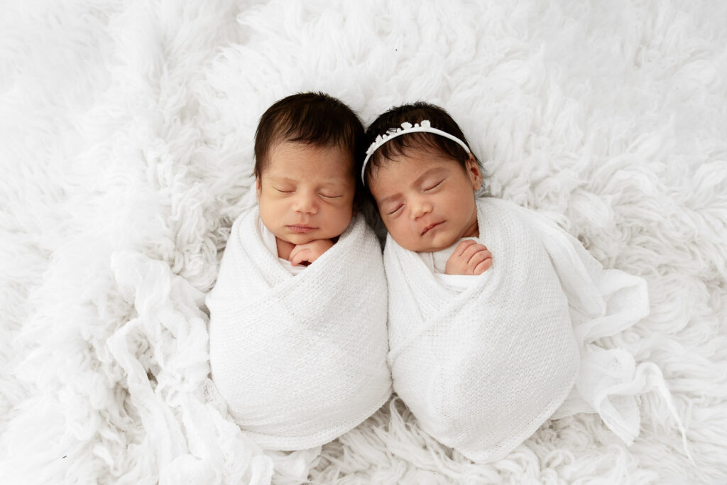Newborn twin babies sleeping swaddled on a white flokati fur