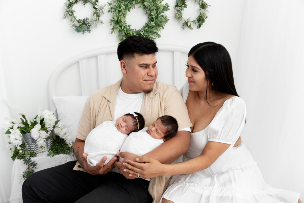 mom and dad holding newborn twins on a white studio lifestyle bed