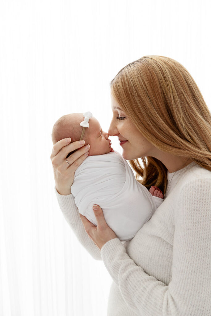 backlit image of mom holding swaddled baby daughter nose to nose