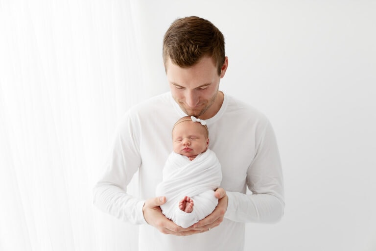sidelit image of dad holding swaddled newborn baby girl with toes peeking out of swaddle
