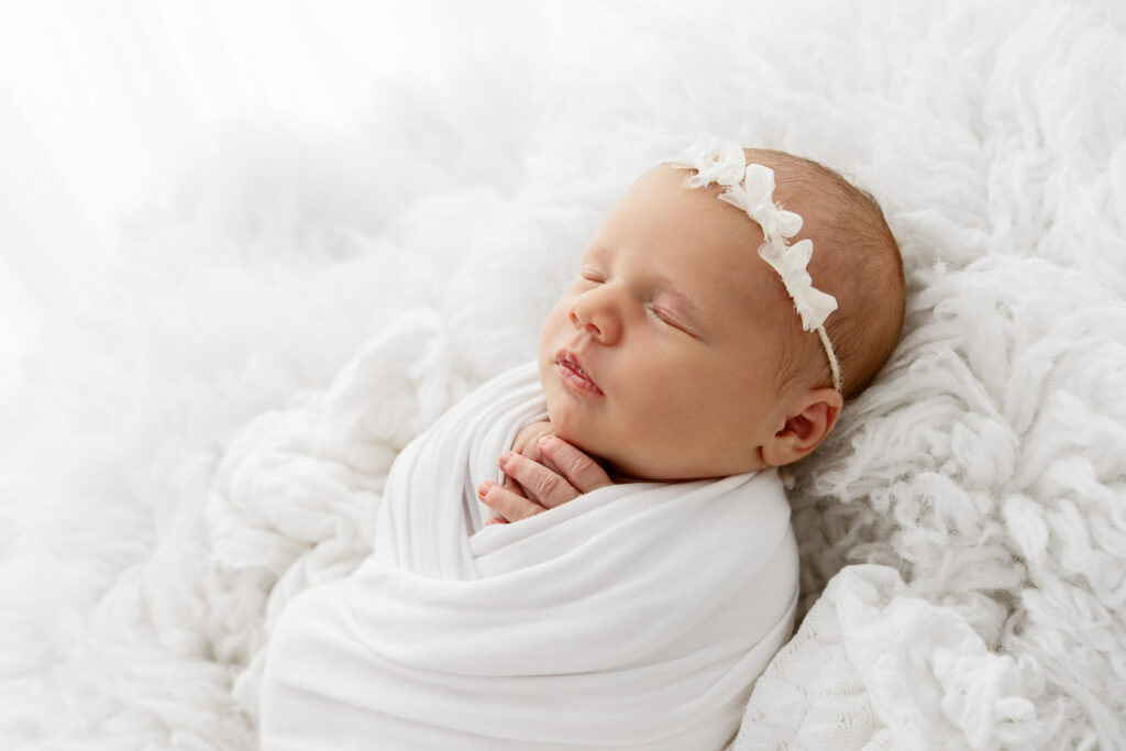 backlit image of newborn baby girl sleeping swaddled on white flokati fur