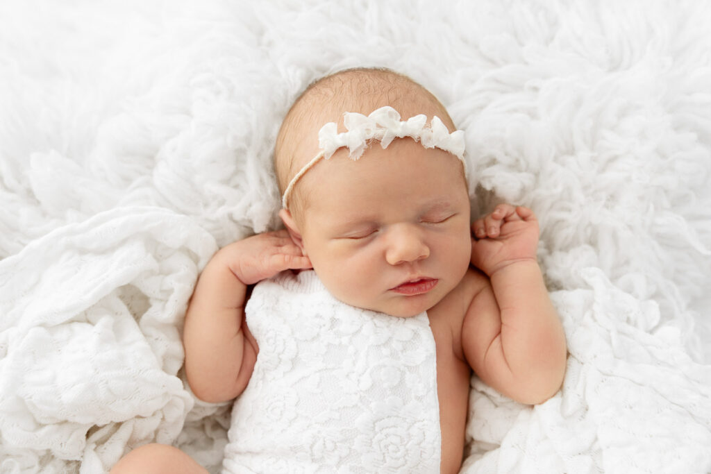 newborn baby girl wearing white romper sleeping on a white flokati fur