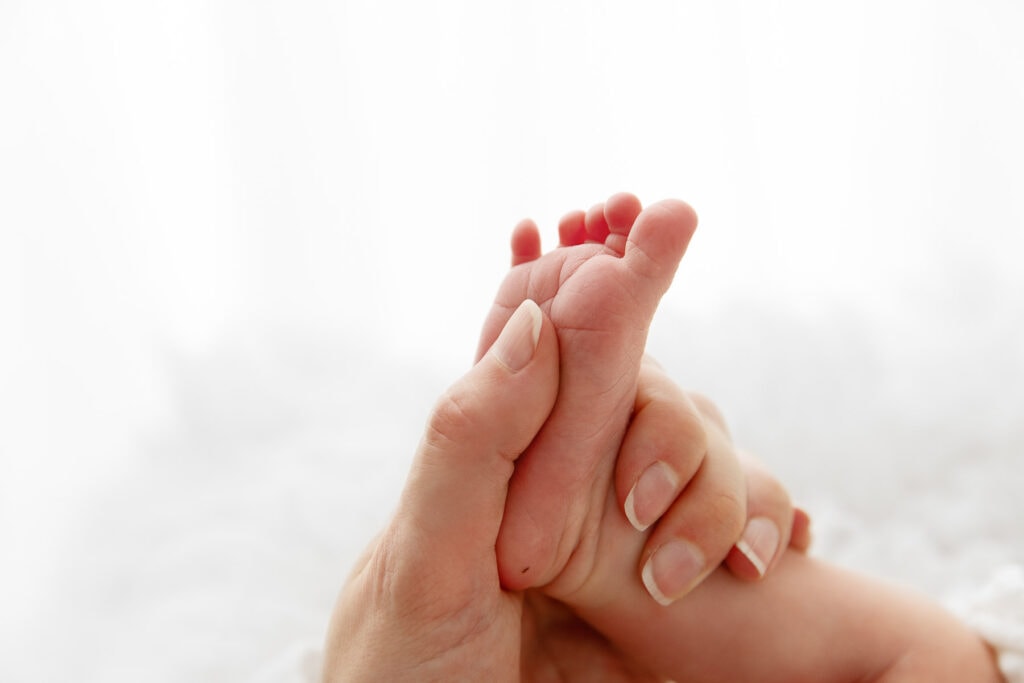 backlit Close up of mom's hand holding newborn baby daughter's foot