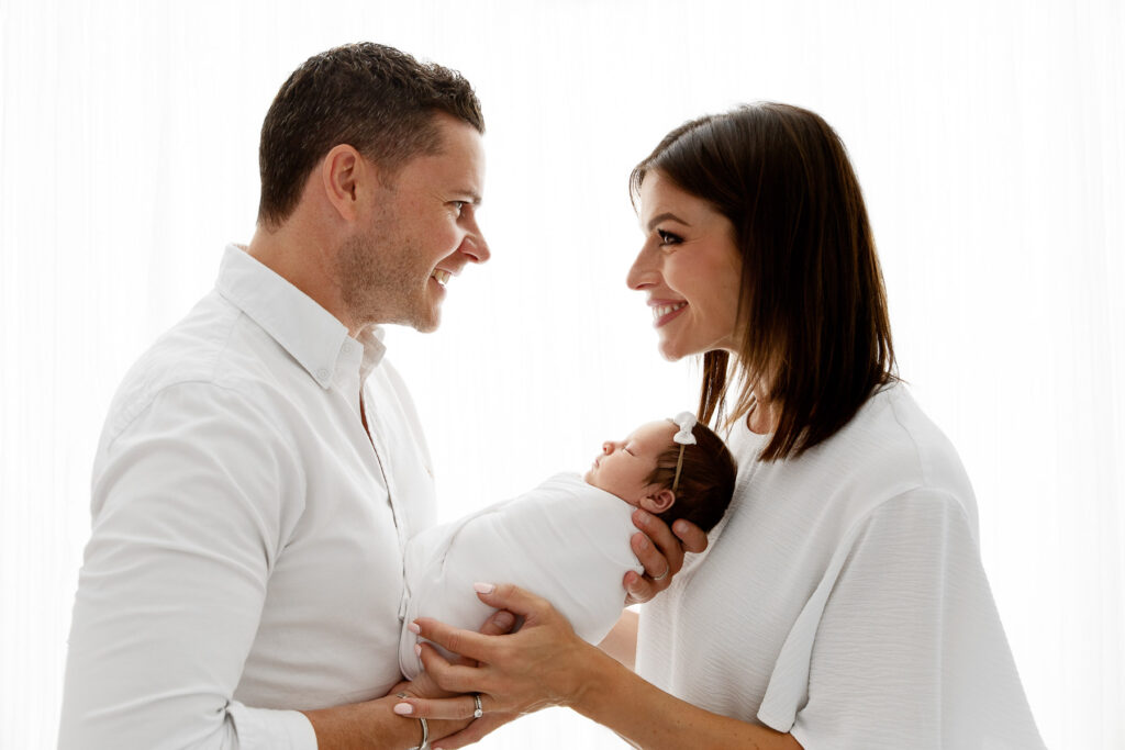 backlit parents holding swaddled newborn baby girl