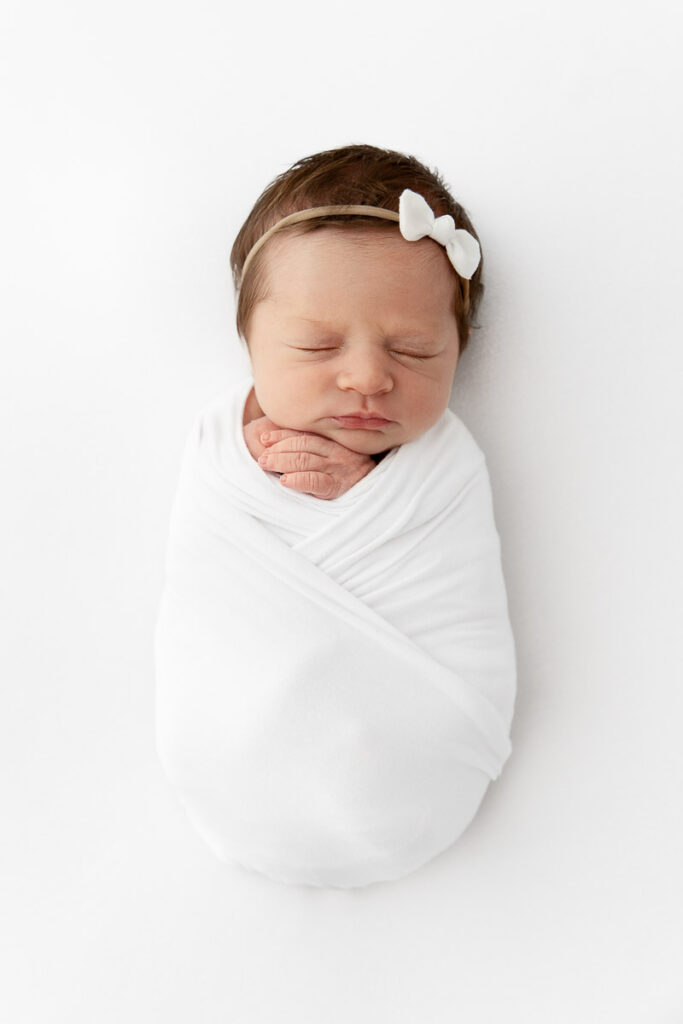 newborn baby girl sleeping swaddled tightly on white beanbag