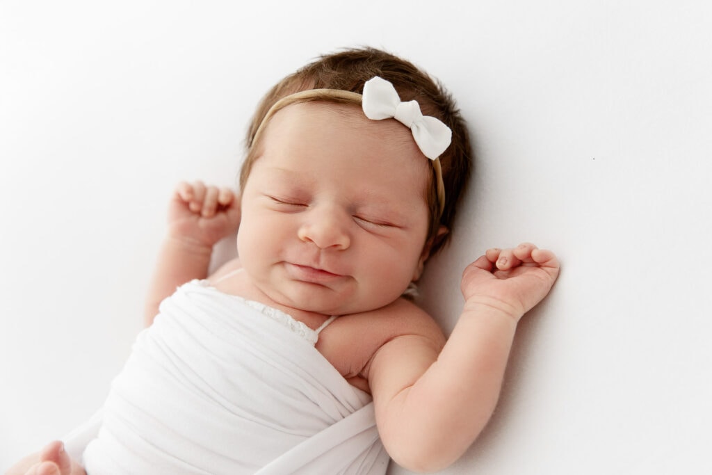 sleeping smiling baby girl with arms above her head in newborn session