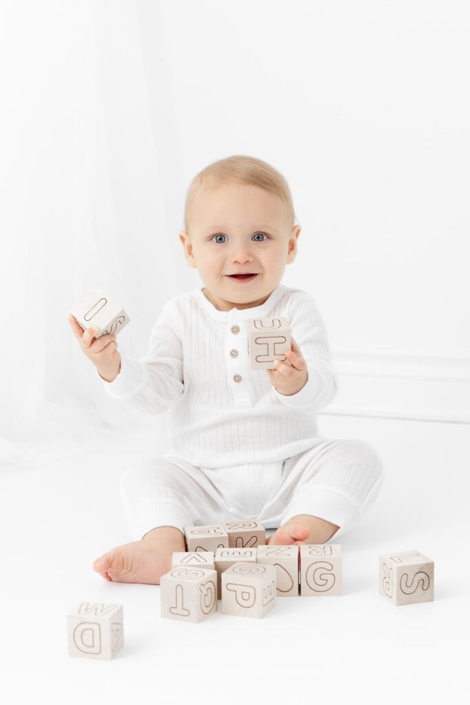 baby boy wearing white romper playing with natural wood letter blocks