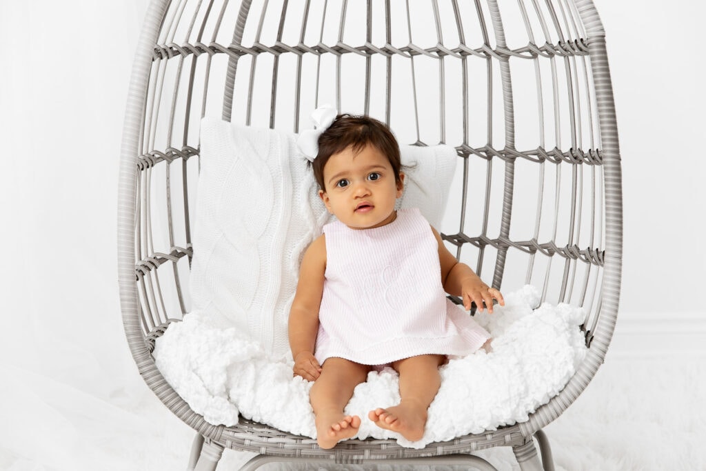 1 year old girl sitting in an egg chair prop