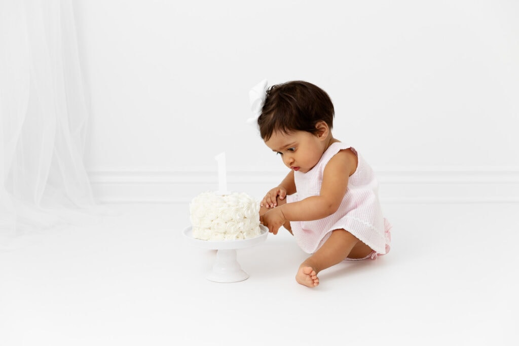 1 year old baby girl poking her finger into a white smash cake