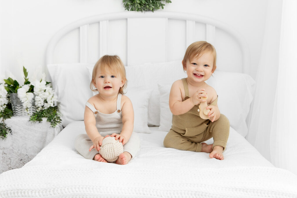 twin 1 year olds sitting together on a white lifestyle bed