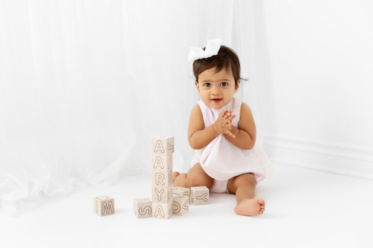 1 year old girl playing with natural wooden blocks in front of a sheer white curtain