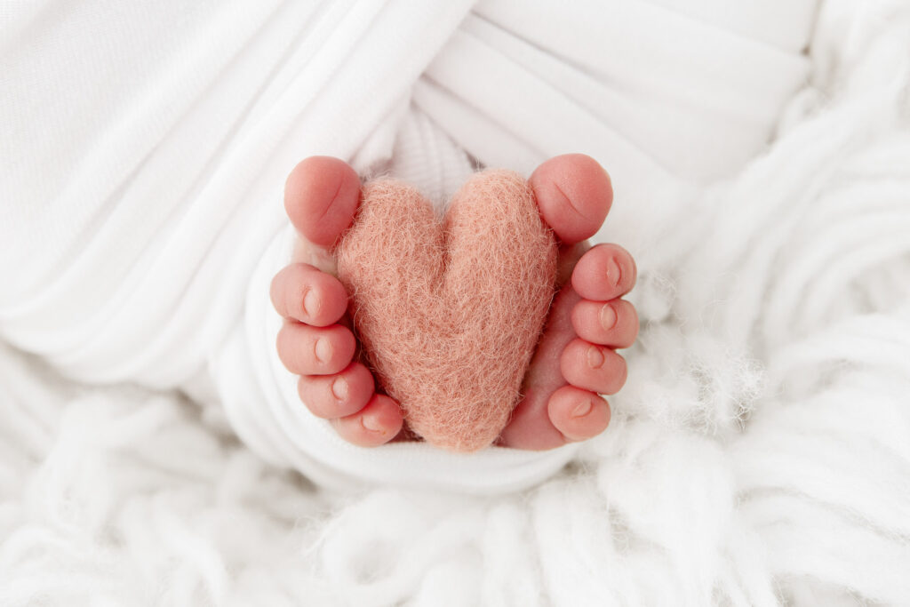close up photo of newborn baby toes holding pink knit heart