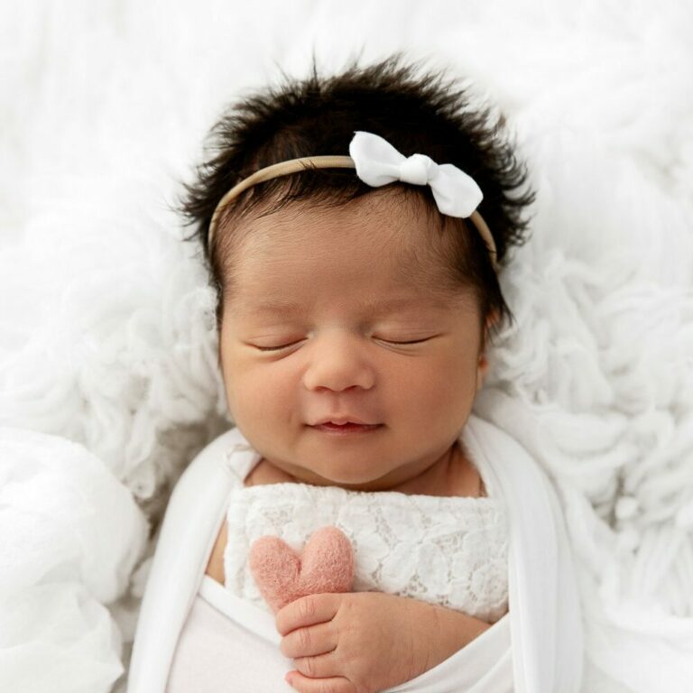 newborn baby girl sleeping on white fur holding pink felt heart