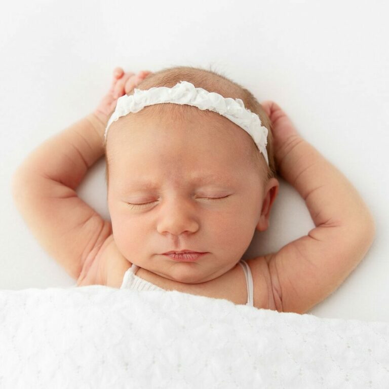 newborn baby girl sleeping on white beanbag with arms above her head