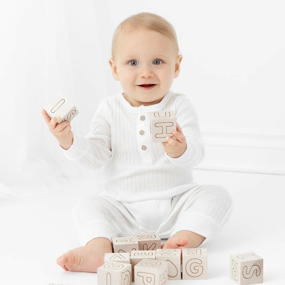 9 month old baby boy wearing long white romper playing with wooden blocks in a white studio