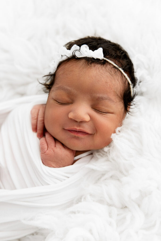 newborn baby girl sleeping wrapped on a white fur during photo session