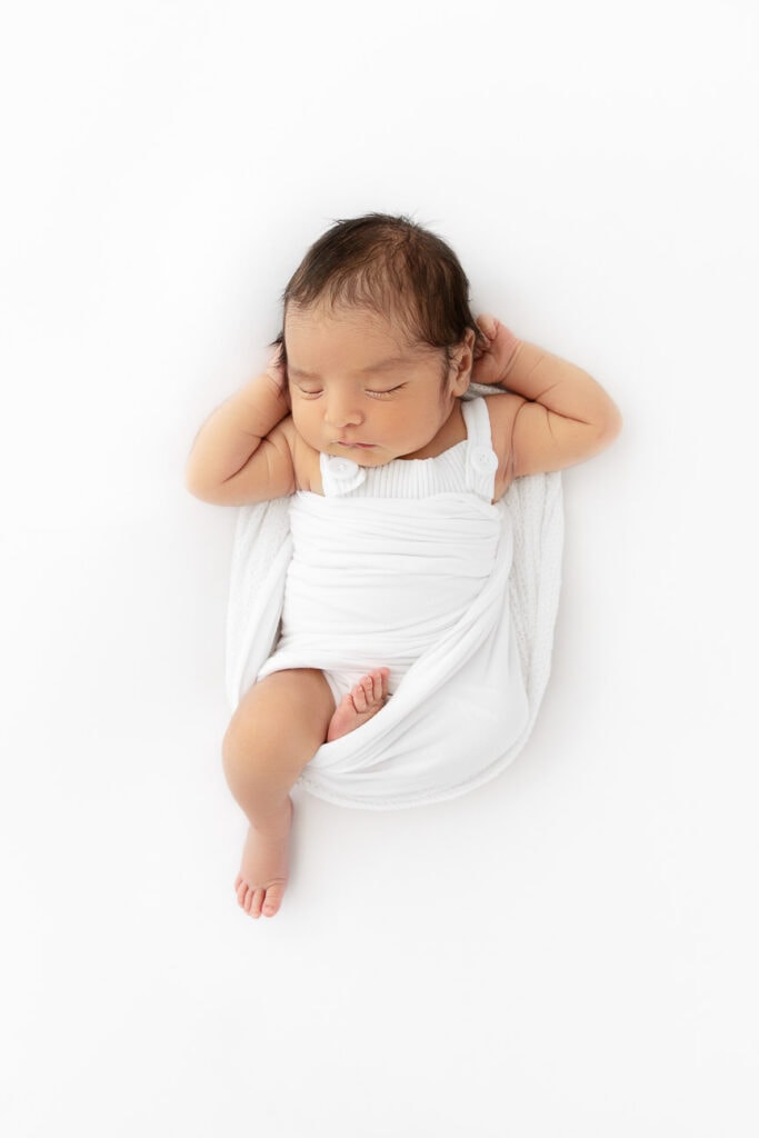 newborn baby boy sleeping on white beanbag with arms behind head