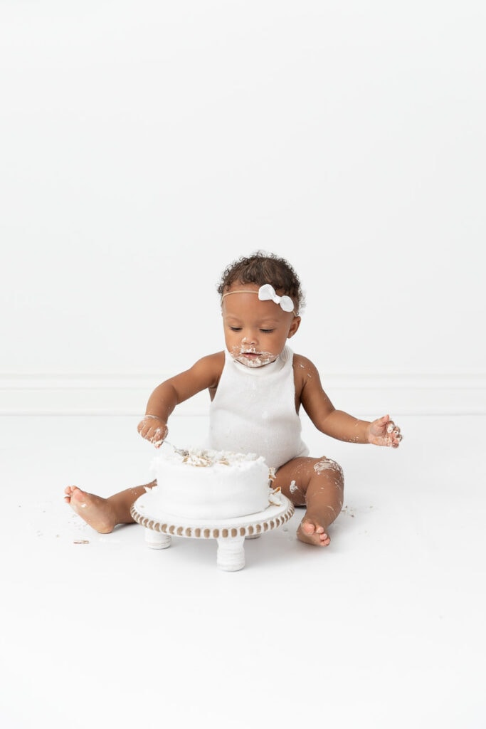 One year old baby girl eating cake with spoon during photo session