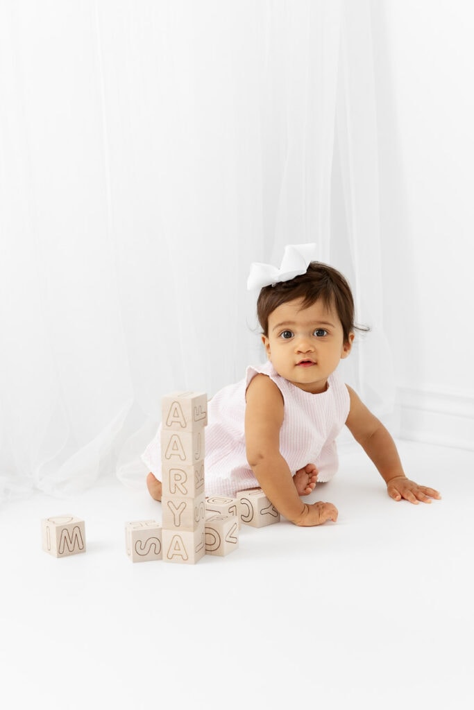 One year baby girl playing with wooden blocks in front of sheer white curtain