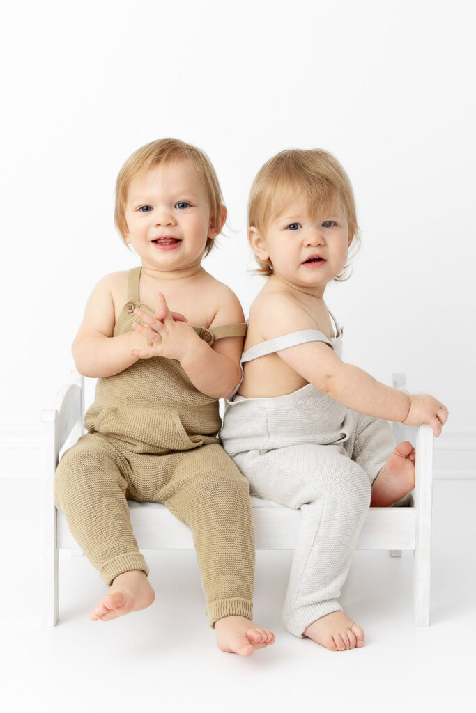 twin 1 year old boys sitting on a white doll bed
