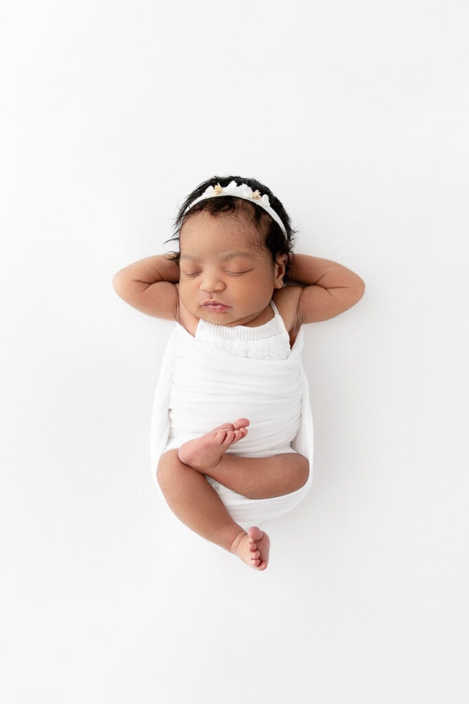 newborn baby girl laying on white beanbag with legs crossed and arms behind head