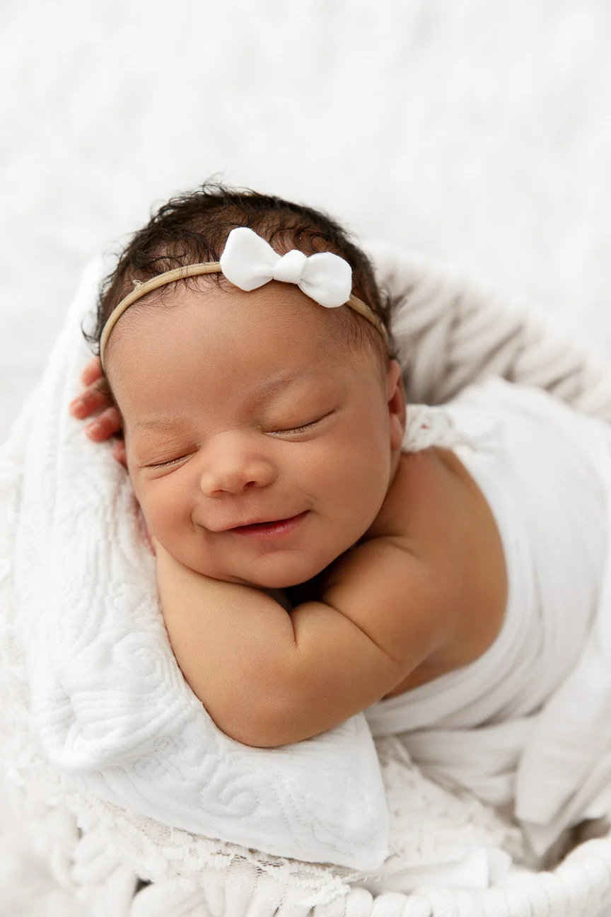newborn baby girl sleeping and smiling in a bucket prop in a white studio
