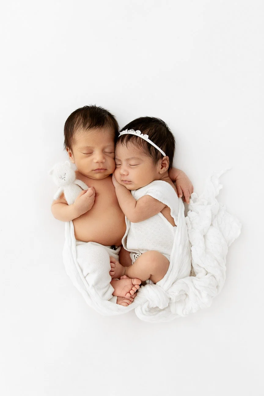 Boy and girl newborn twins snuggled together on a white beanbag