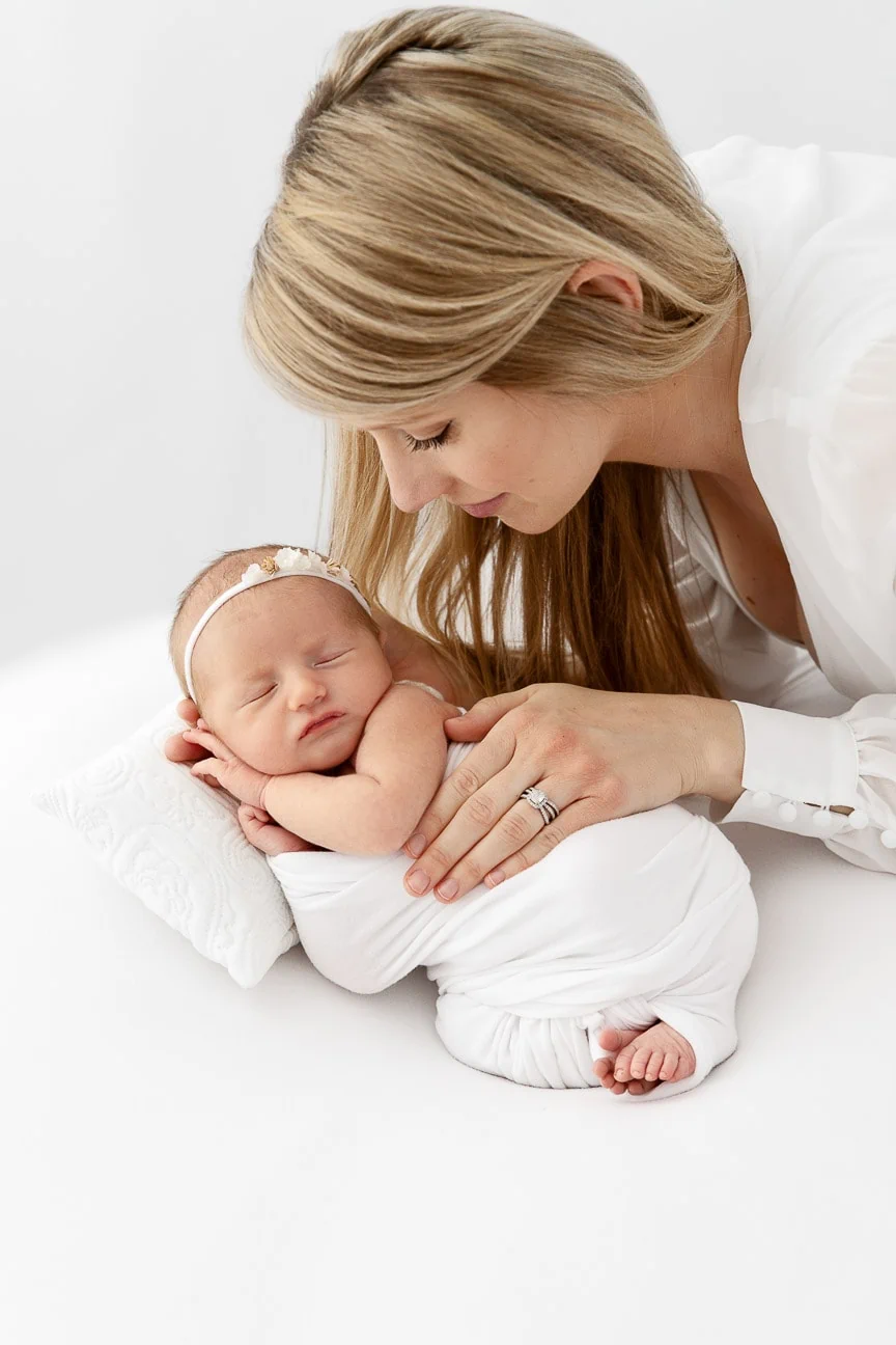 mom holding newborn baby girl sleeping on pillow in a white studio
